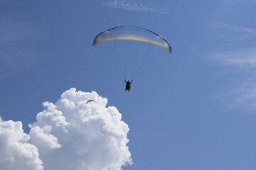 Low-angle shot of a person paragliding under a cloudy blue sky