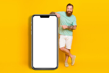 Full length photo of happy promoter young hipster guy beard direct finger phone web social media advert network isolated on yellow color background