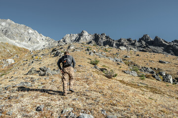 A male tourist with a backpack climbs uphill to a rocky peak. The concept of motivation and...