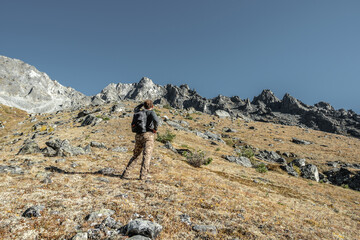 A male tourist with a backpack climbs uphill to a rocky peak. The concept of motivation and...