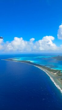 Vertical aerial of Bora Bora islands surrounded by beautiful blue seascape under fluffy clouds