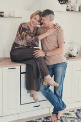  family enjoying tender moment, beautiful happy middle aged woman embracing grey haired man sitting on kitchen table.