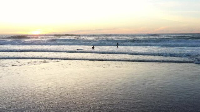Two Surfer friends carving large breaking wave at colorful summer sunset. Surfer amateurs ride a board in the ocean at sunset