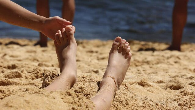 Child, tickling sibling on the beach on the feet with feather, kid cover in sand, smiling, laughing, enjoying some fun