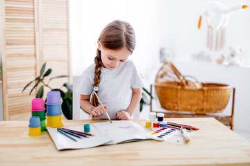 a little girl draws drawings with multicolored paints or learns to draw in a bright children's room at home or in kindergarten, a smiling child, the lifestyle of a preschooler child