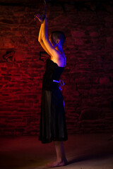 BDSM concept. Woman in black dress with her hands tied and tied to ceiling. Illuminated by duplex...