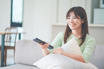リビングのソファに座ってテレビのリモコンを操作する女性