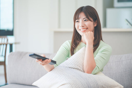 リビングのソファに座ってテレビのリモコンを操作する女性