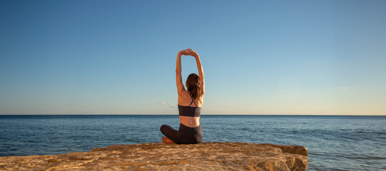 female sitting on rocks by the sea meditating in the sun