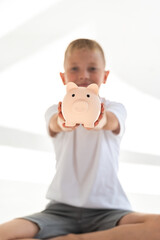A boy with a piggy bank in his hands on a white background. Concept of finances and family budget. Bright and sunny picture.