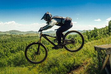 athlete mountainbiker jump drop downhill in flight. against background mountains in green forest