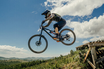 athlete mountain biker jump drop downhill in flight. against background of blue sky and mountains