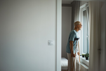 Senior man with crutches spending time alone in his apartment.