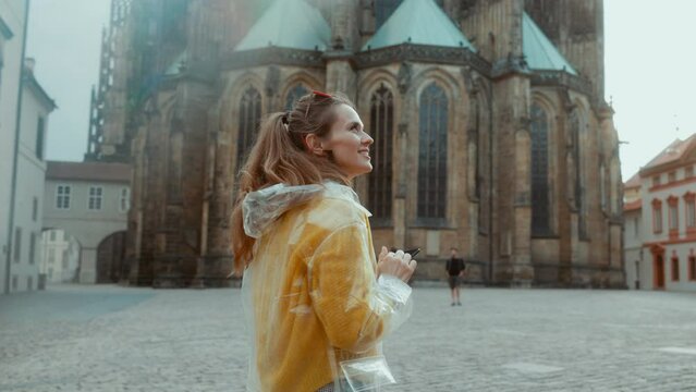 happy stylish traveller woman in yellow blouse and raincoat in Prague Czech Republic with smartphone having excursion.