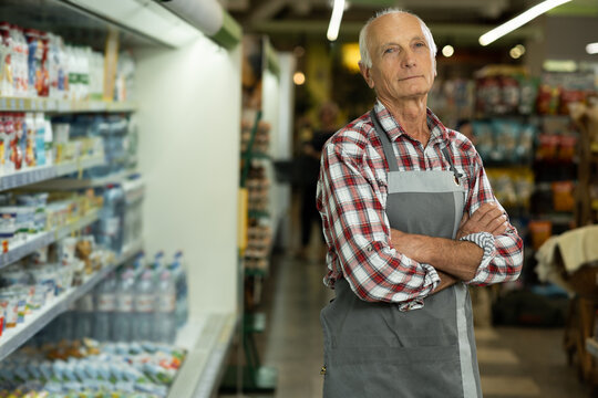 Confident smiling elderly supermarket clerk posing at the shopping mall, looking to the camera. Retail job concept