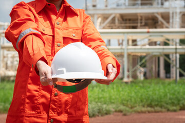 Action of the engineer in orange coverall uniform is holding a white safety helmet with background...