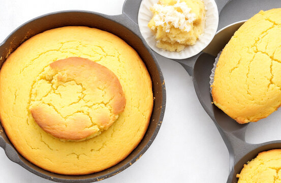 Cornbread muffins and cornbread pone in an iron skillet over white background