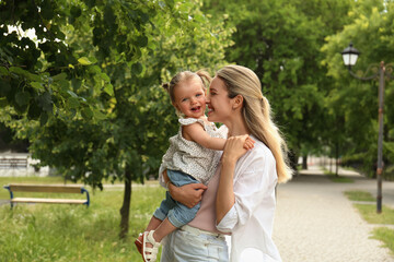 Happy mother with her daughter spending time together in park. Space for text