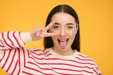 Happy woman showing her tongue and V-sign on orange background