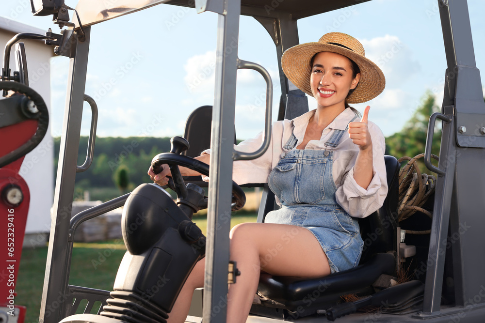 Wall mural Smiling farmer driving loader and showing thumb up outdoors