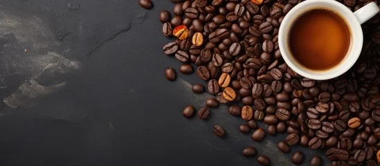 Poster Top view image of a dark stone background with a cup of coffee and coffee beans on a horizontal banner with copy space © AkuAku