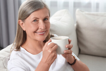 Senior woman with cup of tea on sofa at home