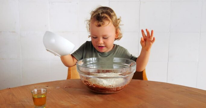 Little boy adds main ingredient, flour, into bowl and starts stirring pancake mix with whisk. His culinary curiosity leads to amusing mishap, he impulsively tasting raw flour mixture