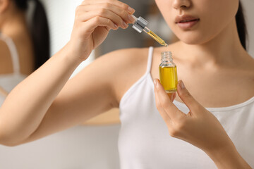 Fototapeta premium Beautiful young woman with bottle of cosmetic serum in bathroom, closeup