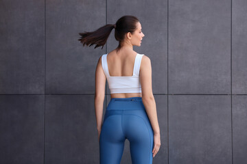 Fototapeta premium Woman in sportswear near dark grey wall, back view