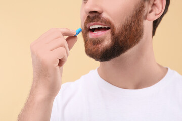 Man taking pill on beige background, closeup