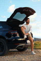 Happy man sitting in trunk of modern car on roadside outdoors