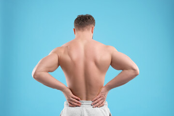Man suffering from back pain on light blue background, back view