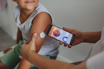 Boy with diabetes checking blood glucose level at home using continuous glucose monitor. - obrazy, fototapety, plakaty