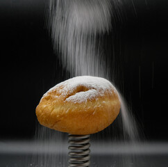 The donut is sprinkled with powdered sugar. Metal spring. Gain weight. Black background. 