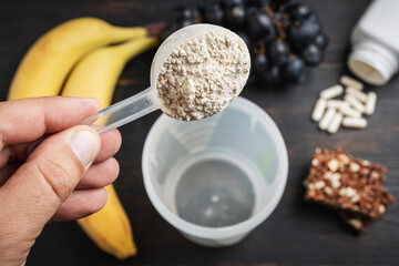 Male hand puts into a shaker scoop portion of whey, soy protein powder. White capsules of amino...