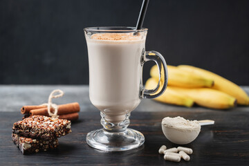 Glass of protein milkshake drink with straw and scoop of whey protein powder, white capsules of...