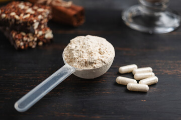 Scoop of whey or soy protein powder, white capsules of amino acids, vitamins, creatine, protein chocolate bar, bodybuilding food supplements, sports nutrition on a dark wooden board