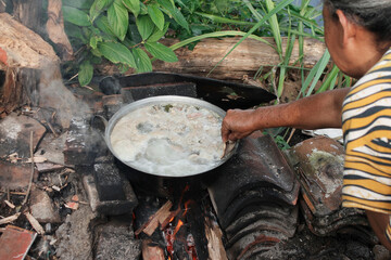 a mother is cooking meat using a pan with campfire