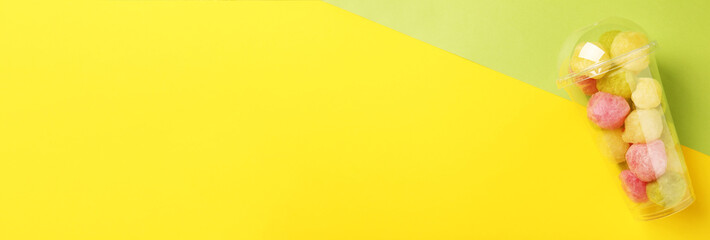 Plastic cup with delicious cotton balls on color background, top view. Banner design with space for text