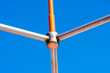 Metal structure of connected pipes in orange and silver color with fastening. Sunny day and Clear, blue sky in the background. Copyspace. Background for quotes