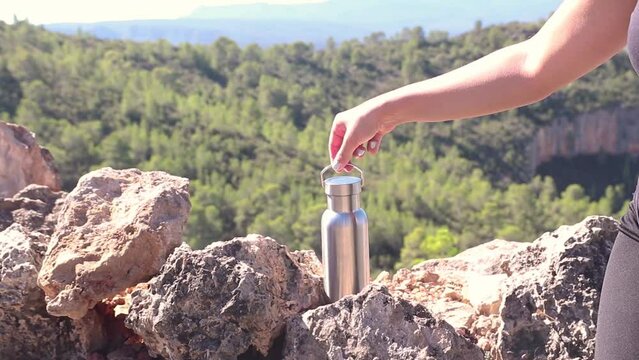 Hand taking an aluminum thermal bottle to hydrate on a hiking trail