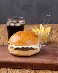 Cheeseburger with mayonnaise over wooden board with french fries and soda