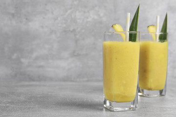 Tasty pineapple smoothie on light gray table, space for text