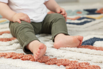 Baby sitting on soft carpet indoors, closeup