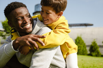 Smiling african man hugging his son while spending time together in park