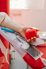 Young woman making blood donation in hospital. A woman donates blood while holding a red heart....