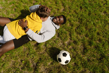 Naklejka premium African man hugging his adopted son while playing football together in park
