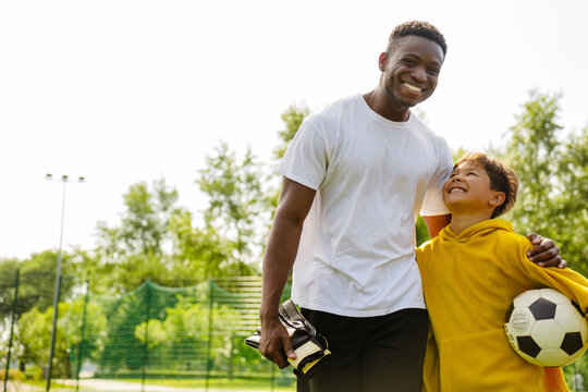African man hugging his adopted son while playing football together in park