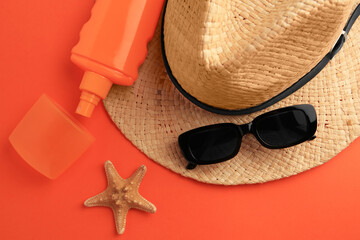 Bottle of sunscreen, starfish and beach accessories on coral background, flat lay