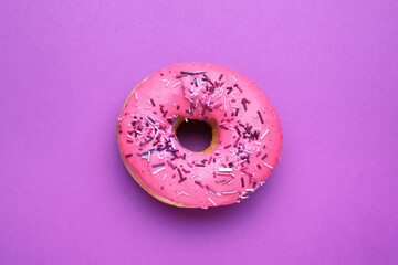 Sweet glazed donut decorated with sprinkles on purple background, top view. Tasty confectionery
